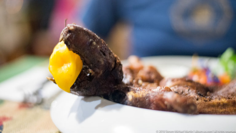 Close-up of a roasted guinea pig head and forelimb with a bright yellow pepper garnish.