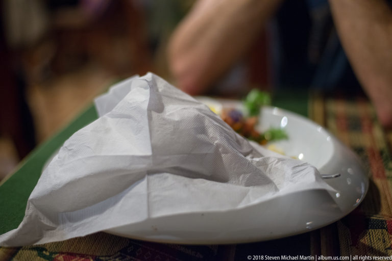 White dinner plate mostly covered by a folded paper napkin, with small portions of food visible at the edge.