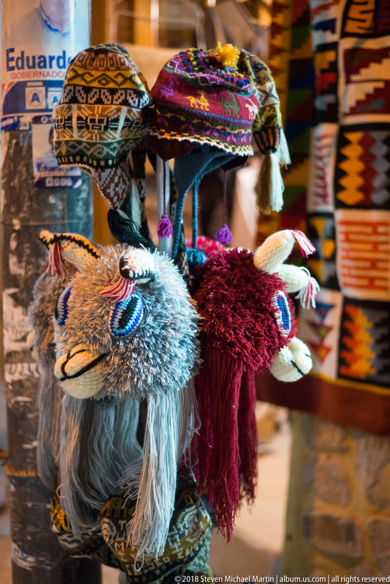 Two shaggy alpaca or llama souvenirs wearing bright woven blankets and tassels in a textile shop.