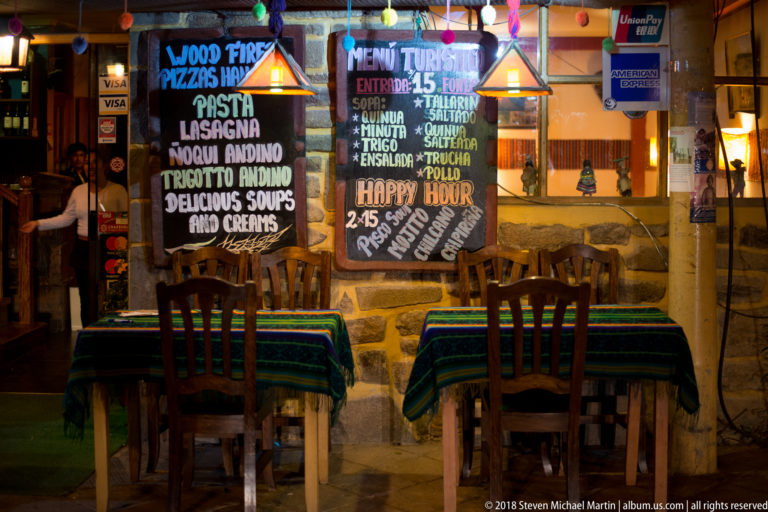 Two empty striped restaurant tables beneath chalkboard tourist menus and warm pendant lights.