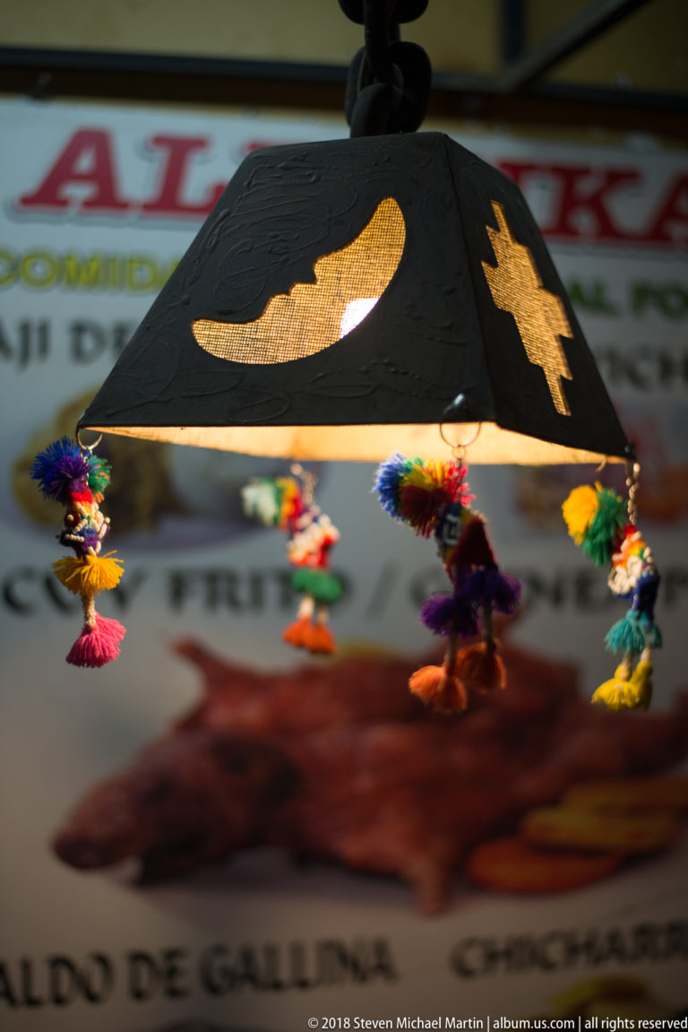 Black hanging lamp with crescent-moon cutouts and small colorful dangling figures beneath the shade.