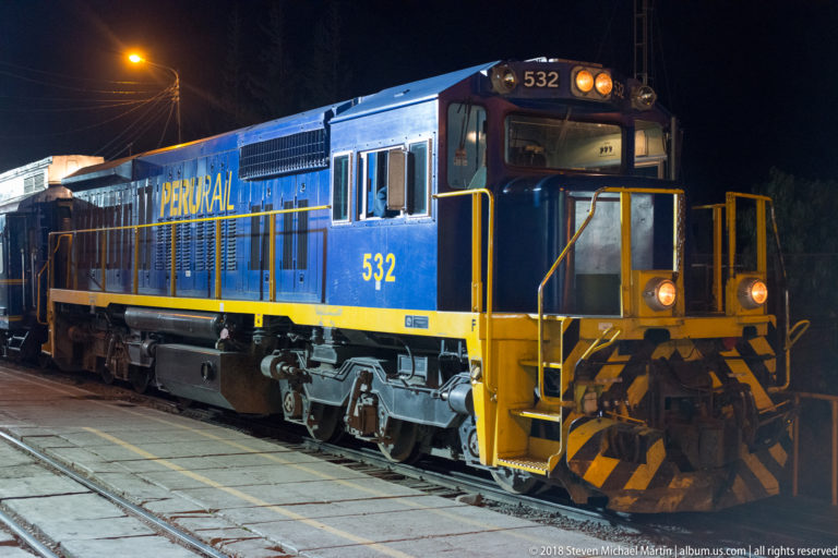 Blue-and-yellow PeruRail diesel locomotive number 532 standing on railway tracks at night.