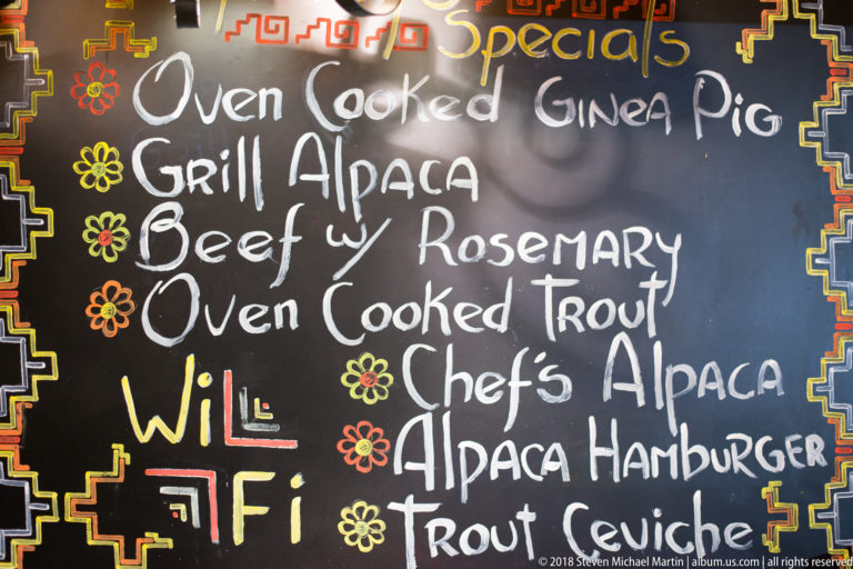 Chalkboard specials menu listing guinea pig, grilled alpaca, beef, trout, alpaca hamburger, and trout ceviche.