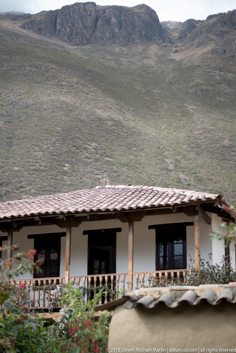 White lodging building with tiled roof and timber balcony below a broad dry Andean mountain slope.
