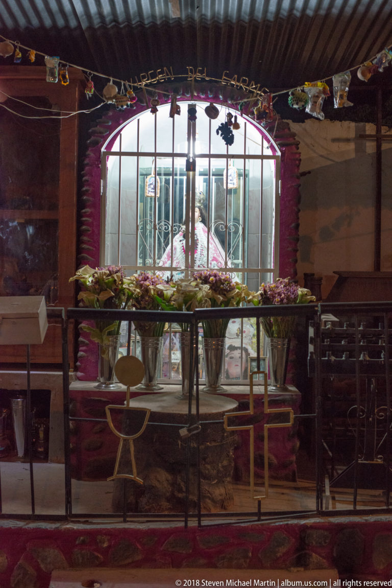Arched barred window decorated with flowers, with chairs and a small table visible inside at night.