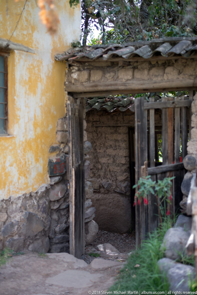 Weathered wooden gateway beside a yellow plaster wall and rough stone masonry in a garden setting.
