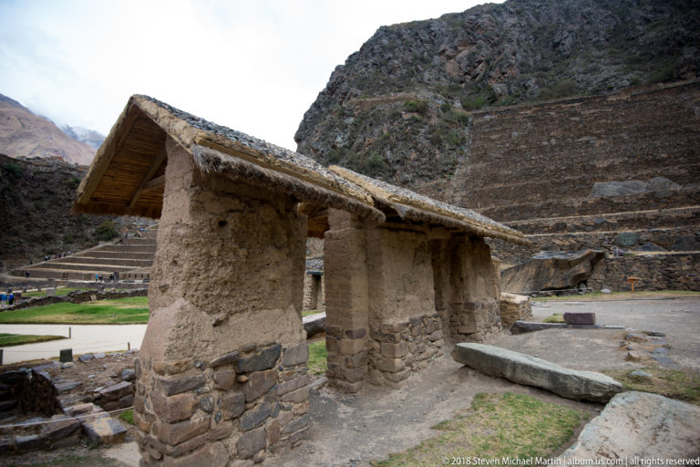 Small adobe and stone building with a steep thatched roof inside the Ollantaytambo archaeological complex.