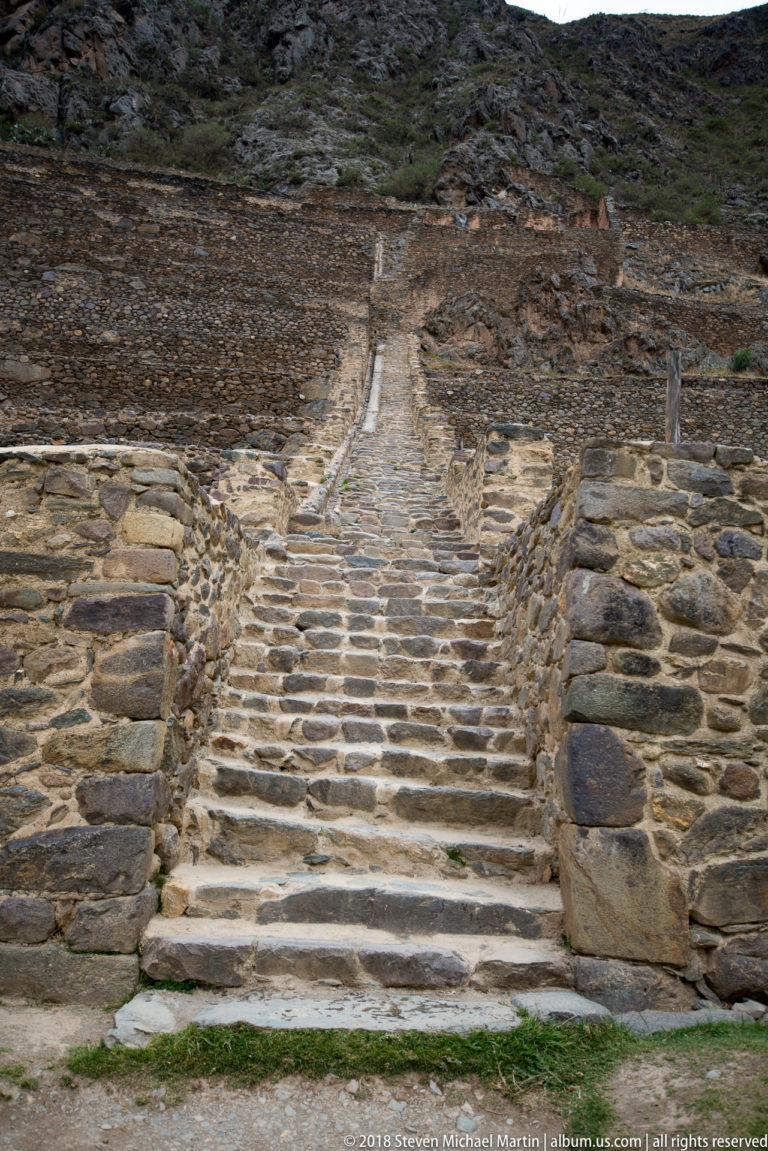 Broad stone staircase ascending between retaining walls on the Ollantaytambo terrace slope.