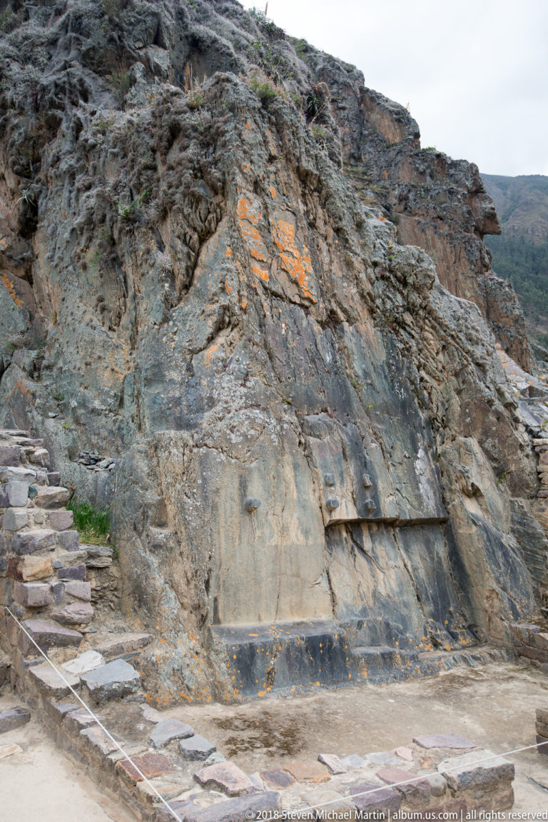 Large worked rock face with horizontal cuts beside a stone staircase at Ollantaytambo.