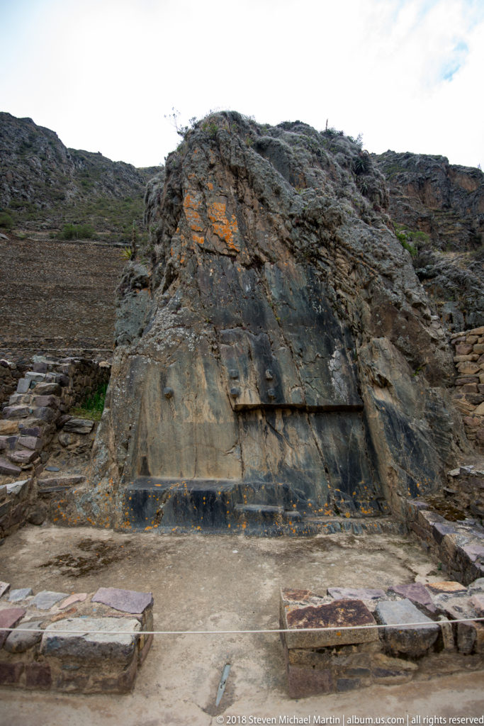 Large rock outcrop with broad smoothed faces, cut lines, and low masonry at the Ollantaytambo archaeological site.