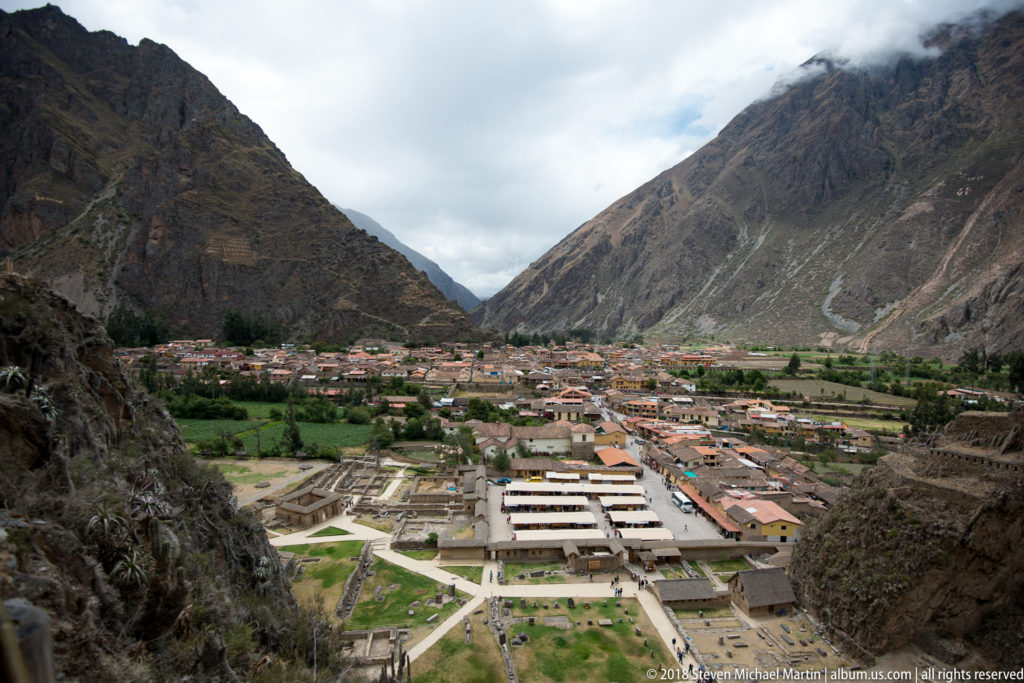 Panoramic view from the ruins over lower archaeological foundations, Ollantaytambo town, and steep mountain walls.