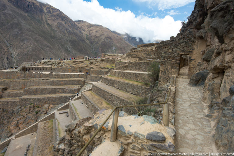 Narrow stone path runs beside exposed bedrock and stepped terrace walls descending across the mountainside.