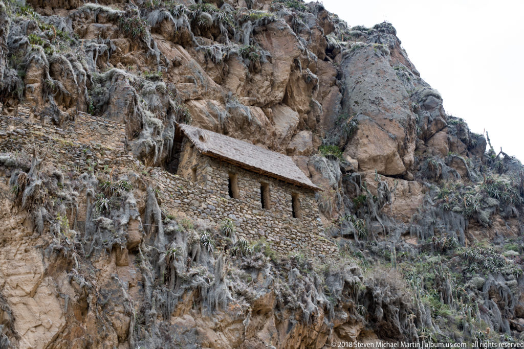 Long roofed stone storehouse with narrow openings built high into the rocky Pinkuylluna hillside above Ollantaytambo.