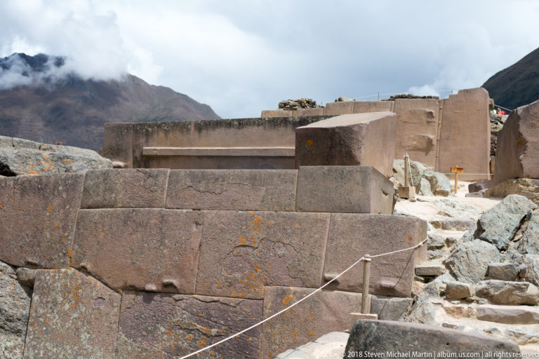 Large reddish fitted Inca stone blocks beside rough natural bedrock, with additional monumental masonry beyond.