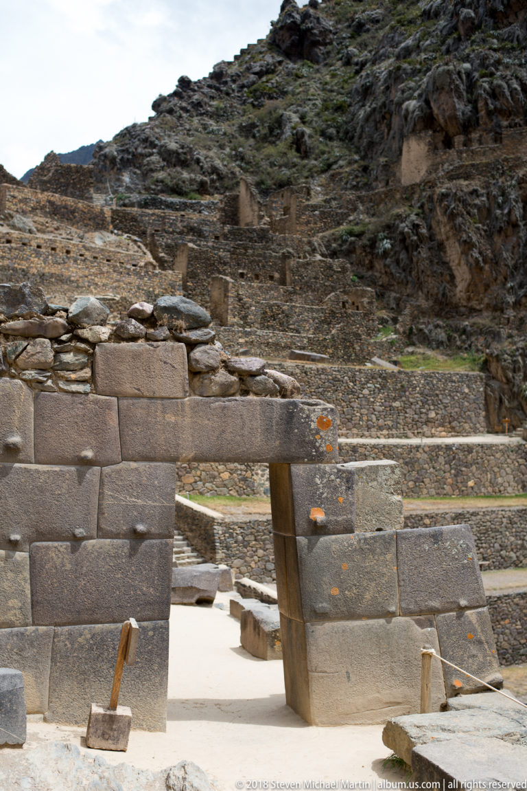 Large fitted-stone doorway with horizontal lintel set within rougher masonry, with terraces rising behind it.