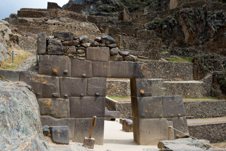 Trapezoidal stone doorway with massive fitted jambs and lintel, backed by terraced walls on the mountainside.