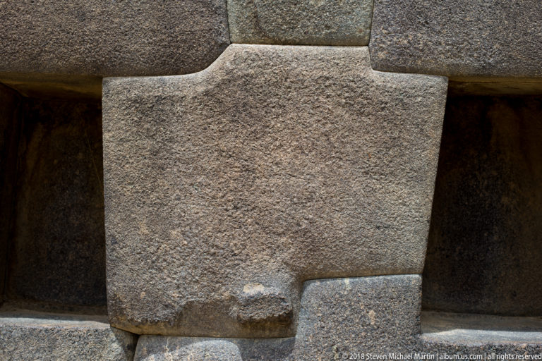 Large dressed Inca stone block with a stepped upper edge and small projecting boss, tightly fitted between neighboring blocks.