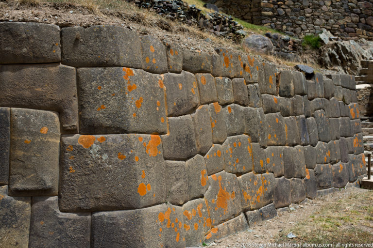 Close view of tightly fitted polygonal Inca stone blocks with projecting bosses and patches of orange lichen.