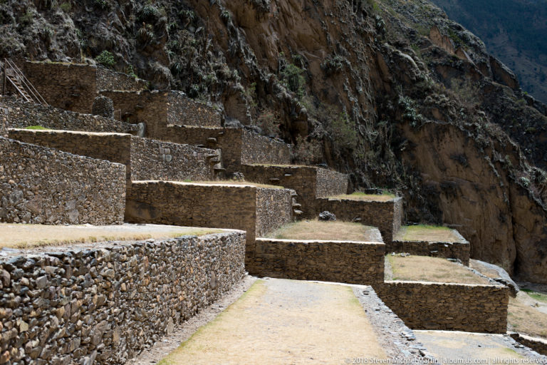 Series of narrow stone-faced terraces stepping upward along a steep rocky mountainside at Ollantaytambo.