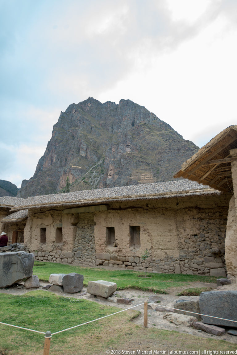 Long low building with a thatched roof and small openings beneath the mountain at Ollantaytambo.