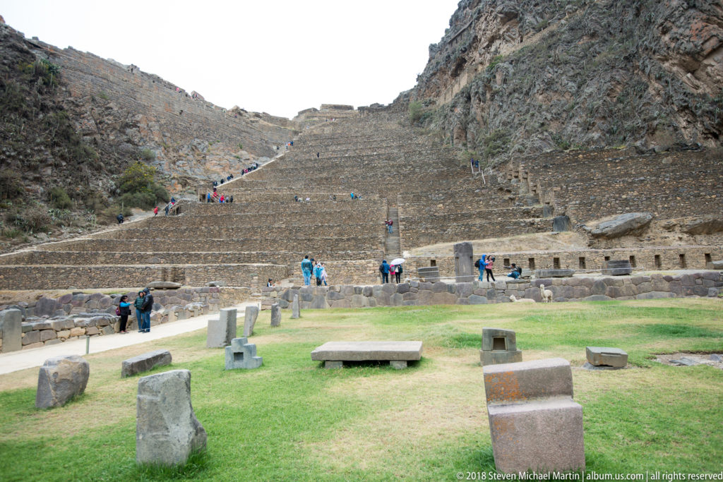 Steep Temple Hill terraces with visitors and large dressed stone blocks scattered across the grassy foreground.
