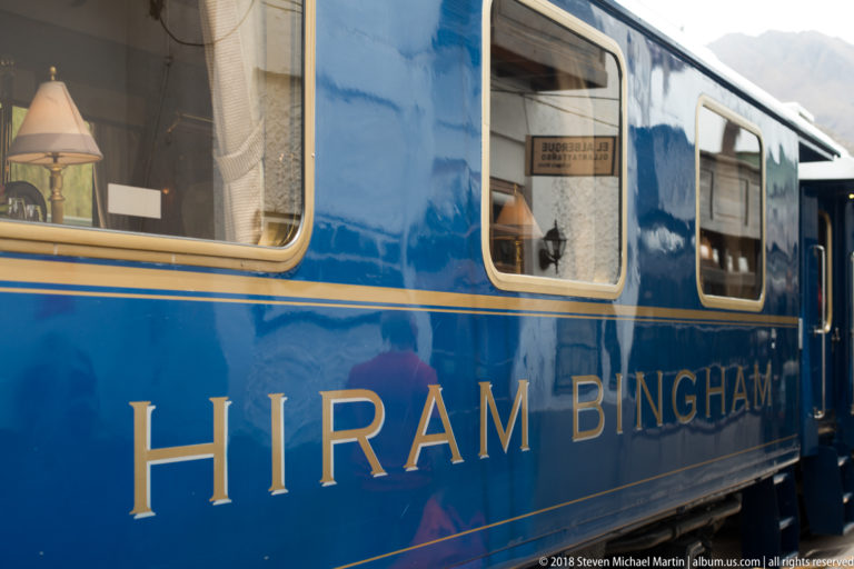 Polished blue Hiram Bingham passenger carriage with large gold lettering and windows revealing lamps inside.