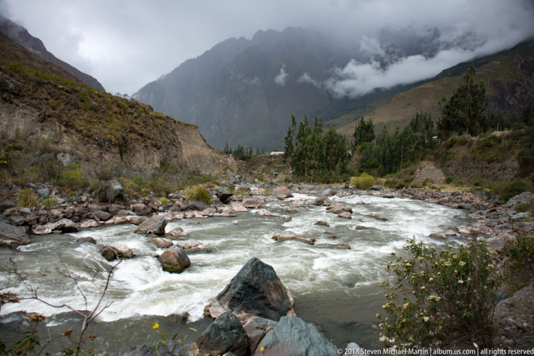 Whitewater river with large boulders below dark mountain peaks partly covered by low cloud.
