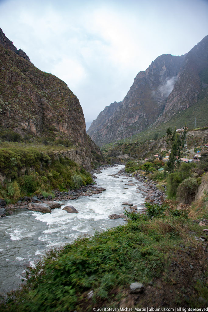 Broad rocky river bending between steep Andean slopes with scattered settlement in the distance.