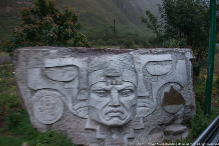 Weathered concrete relief with a stylized face and geometric motifs beside the railway.