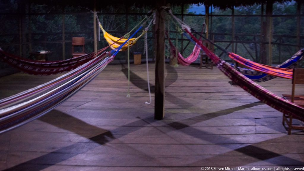 Several brightly colored woven hammocks suspended from timber posts over a large wooden lodge platform.