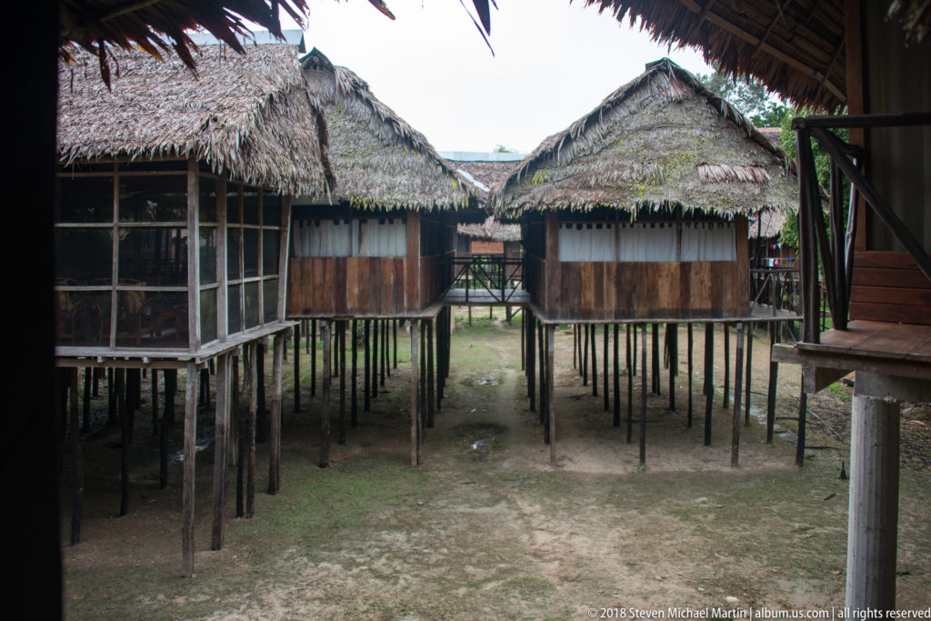 Palm-thatched wooden cabins raised on many timber posts around an open sandy courtyard at Tuhauyo Lodge.