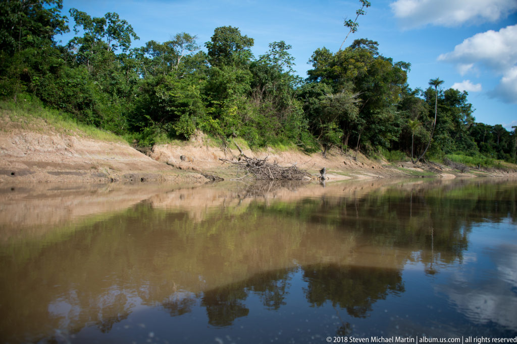 Calm brown Tuhauyo River curving beside an exposed sediment bank topped by dense green forest.