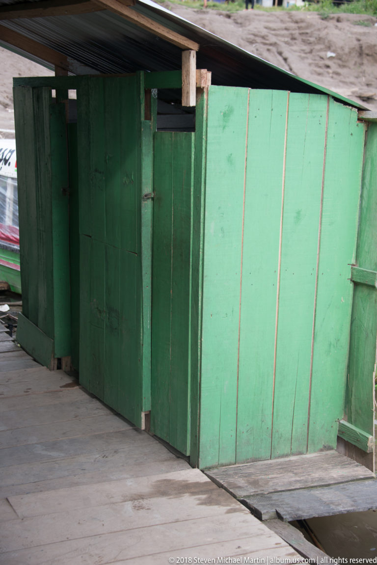 Green-painted plank building with closed wooden doors and a raised board walkway along its exterior.