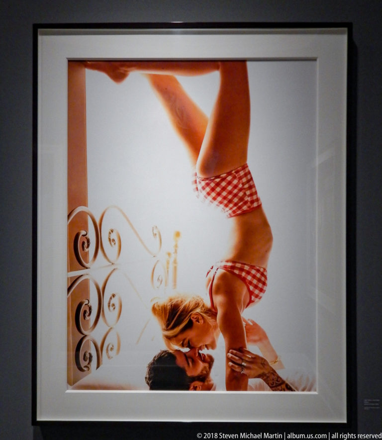 Woman in a red-and-white checked bikini posed upside down beside ornate white metal furniture.