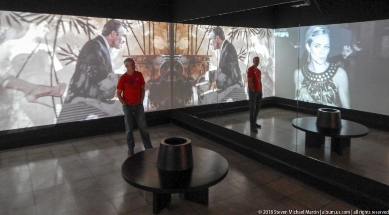 Visitor and mirror reflection inside a gallery wrapped with black-and-white fashion projections and a circular low display.