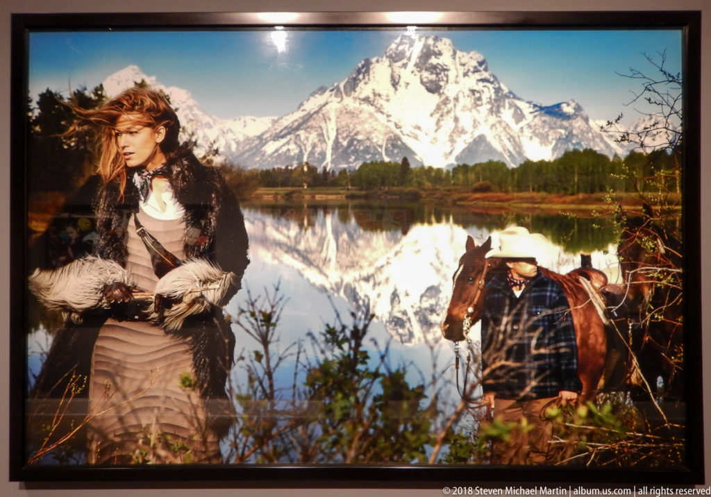 Fashion photograph of a woman beside a saddled horse at a lake with a snowcapped mountain reflected behind them.
