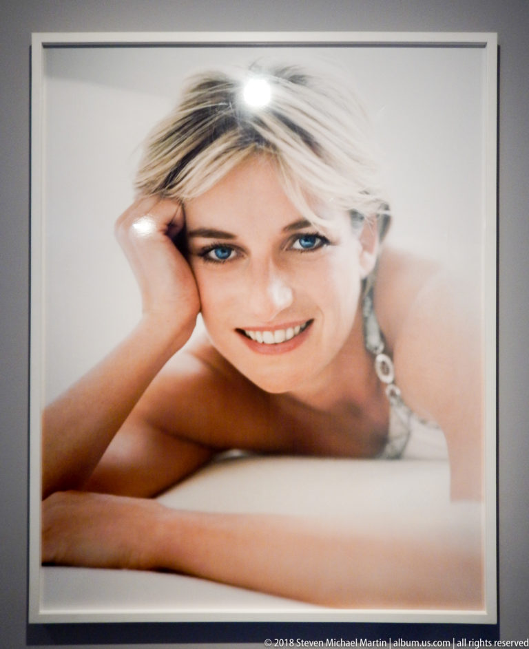 Close color portrait of Diana, Princess of Wales, smiling with one hand supporting her head against a pale background.