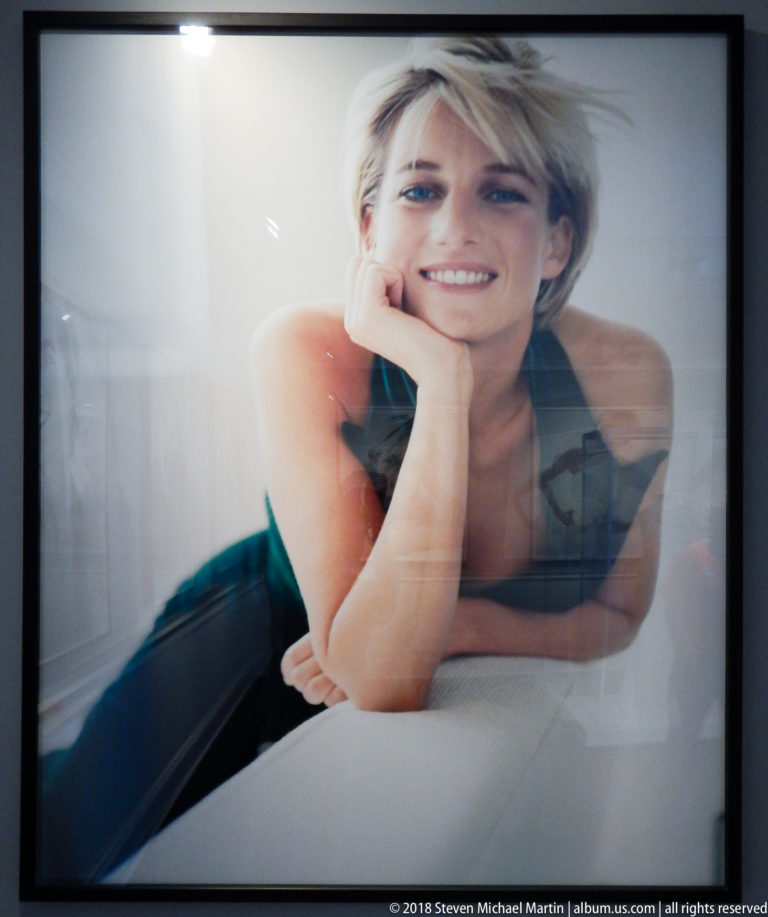 Diana, Princess of Wales, reclines against a pale background, smiling with her head resting on one hand.