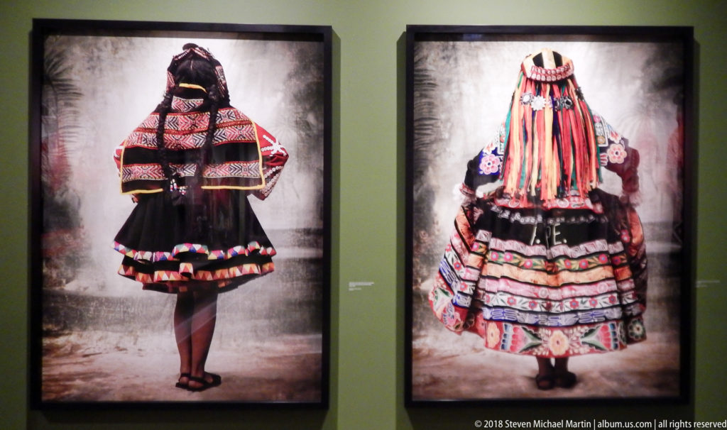 Two framed rear-view portraits of traditional Peruvian dress, one dark and geometric and one layered with colorful ribbons.