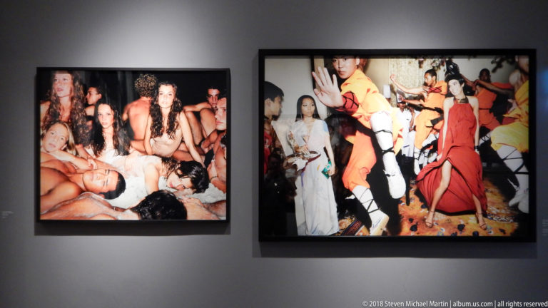Two framed color photographs of crowded social scenes, one intimate and partially dressed, the other filled with brightly costumed figures.
