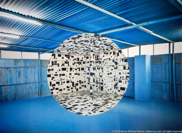 Centered black-and-white patterned enclosure in a blue room, divided by a slender central support.