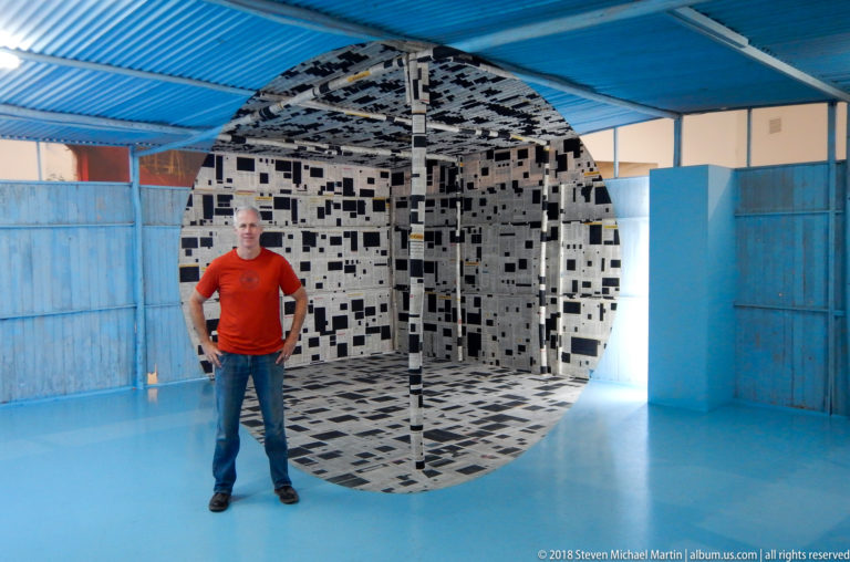Visitor centered before a black-and-white patterned cube installation in a blue gallery.