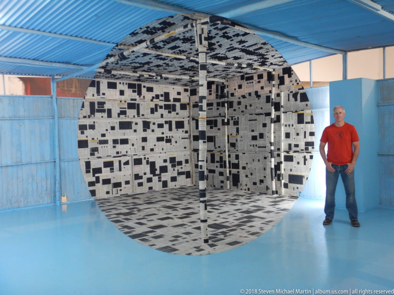 Frontal view of black-and-white patterned installation with a visitor standing beside its circular-looking opening.