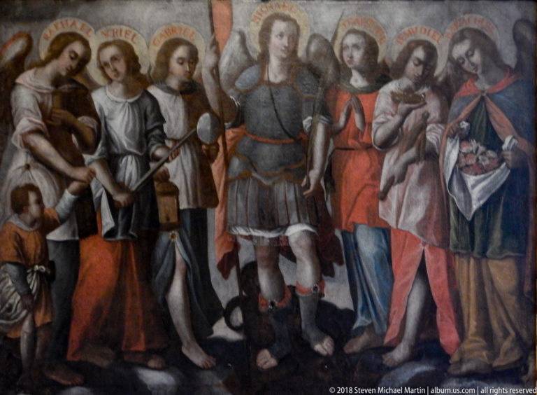 Close detail of a religious painting with an armored central figure and several richly dressed sacred figures bearing inscriptions above.