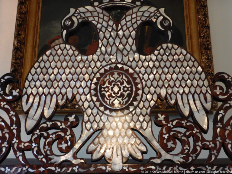 Close detail of two symmetrical white shell-inlaid birds surrounding a circular floral medallion on dark wood.