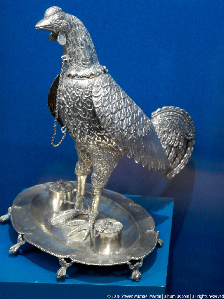 Large embossed silver bird with raised wings standing on an oval footed tray against a blue display background.