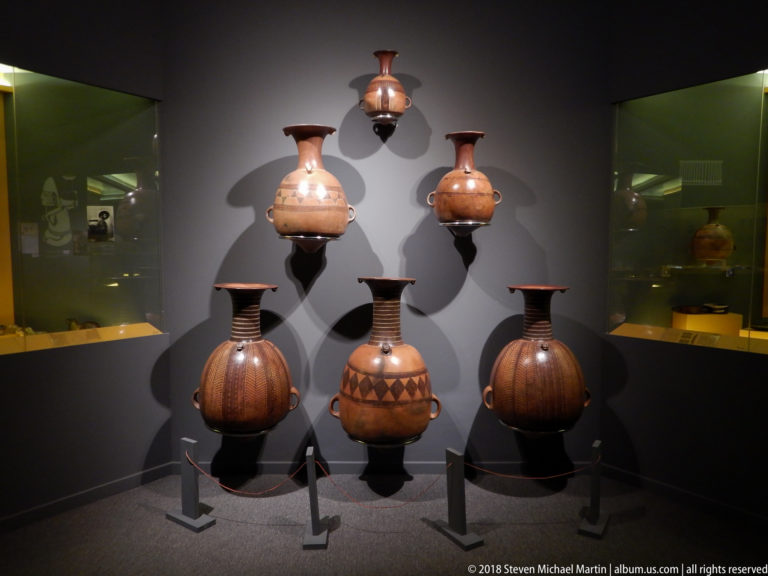 Six reddish-brown ceramic vessels displayed in two rows, including globular jars with ribbed and geometric decoration.