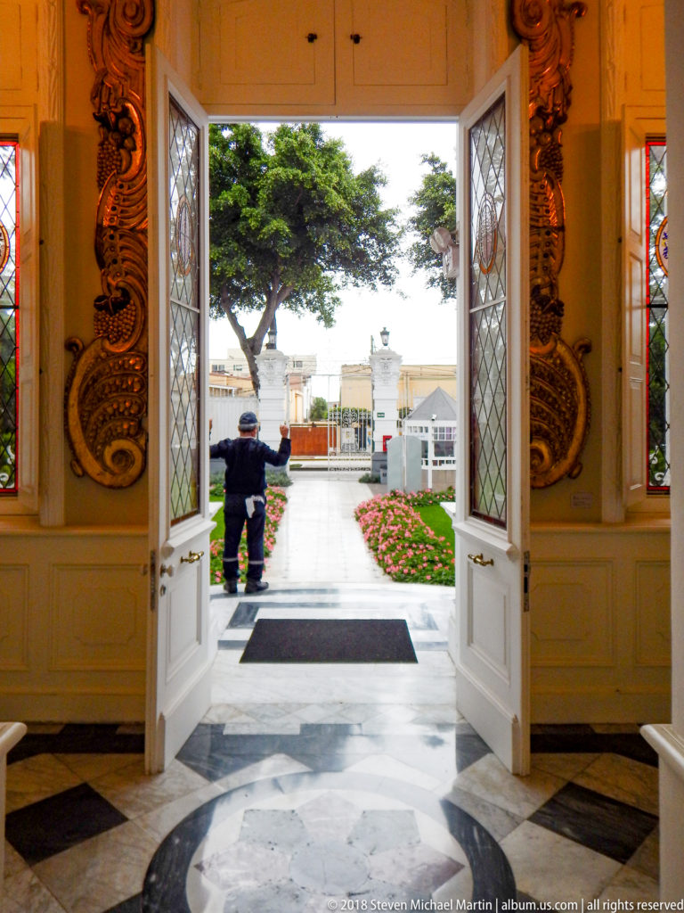 Open white double doors with stained glass leading from the museum interior to a garden court, with a person outside.