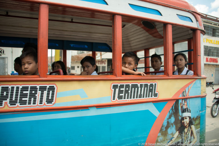 Schoolchildren looking through open windows of a brightly painted bus marked “Terminal.”