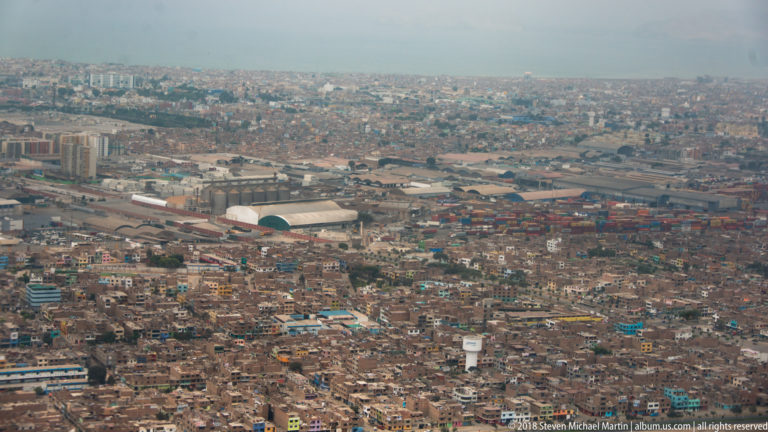 Aerial view over a densely built low-rise city with warehouses, roads, and industrial facilities.